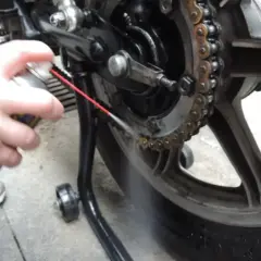 Mano spruzza spray sulla catena della moto per pulirla.