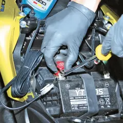 Mani guantate usano una chiave per staccare la batteria moto.
