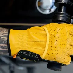 Mano tatuata con guanti Biltwell gialli traforati, pronti per un giro in moto.