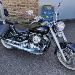 Yamaha Dragstar 650 Custom nera, con borse in pelle borchiate e pneumatici a banda bianca, pronta per un viaggio.