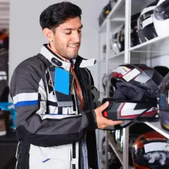 Uomo in giacca da moto sceglie un casco. La taglia XS del casco corrisponde a una misura piccola, ideale per teste di dimensioni ridotte.