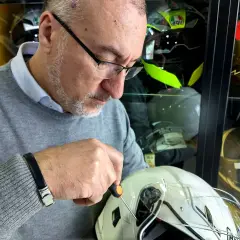 Uomo con cacciavite regola la visiera di un casco bianco, assicurandosi che il casco debba avere la visiera priva di graffi.