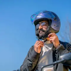 Uomo con casco blu metallizzato, pronto per un giro in moto. Il casco taglia 58 a cosa corrisponde? Probabilmente una misura media, perfetta per lui.