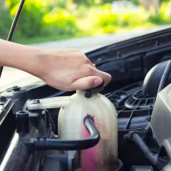 Mano che svita il tappo del serbatoio del liquido refrigerante per la pulizia del radiatore.
