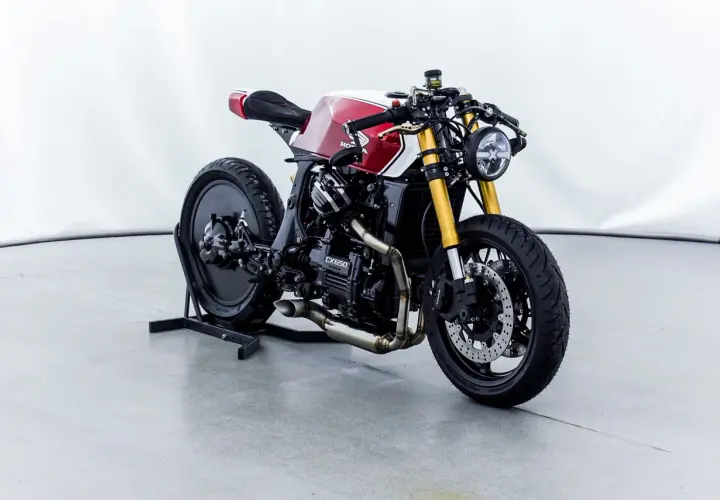 Honda CX650 custom cafe racer, rossa e bianca, con forcella dorata e scarico modificato. Un vero gioiello su due ruote.