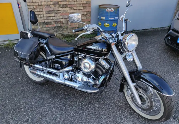 Yamaha Dragstar 650 Custom nera, con borse in pelle borchiate e pneumatici a banda bianca, pronta per un viaggio.