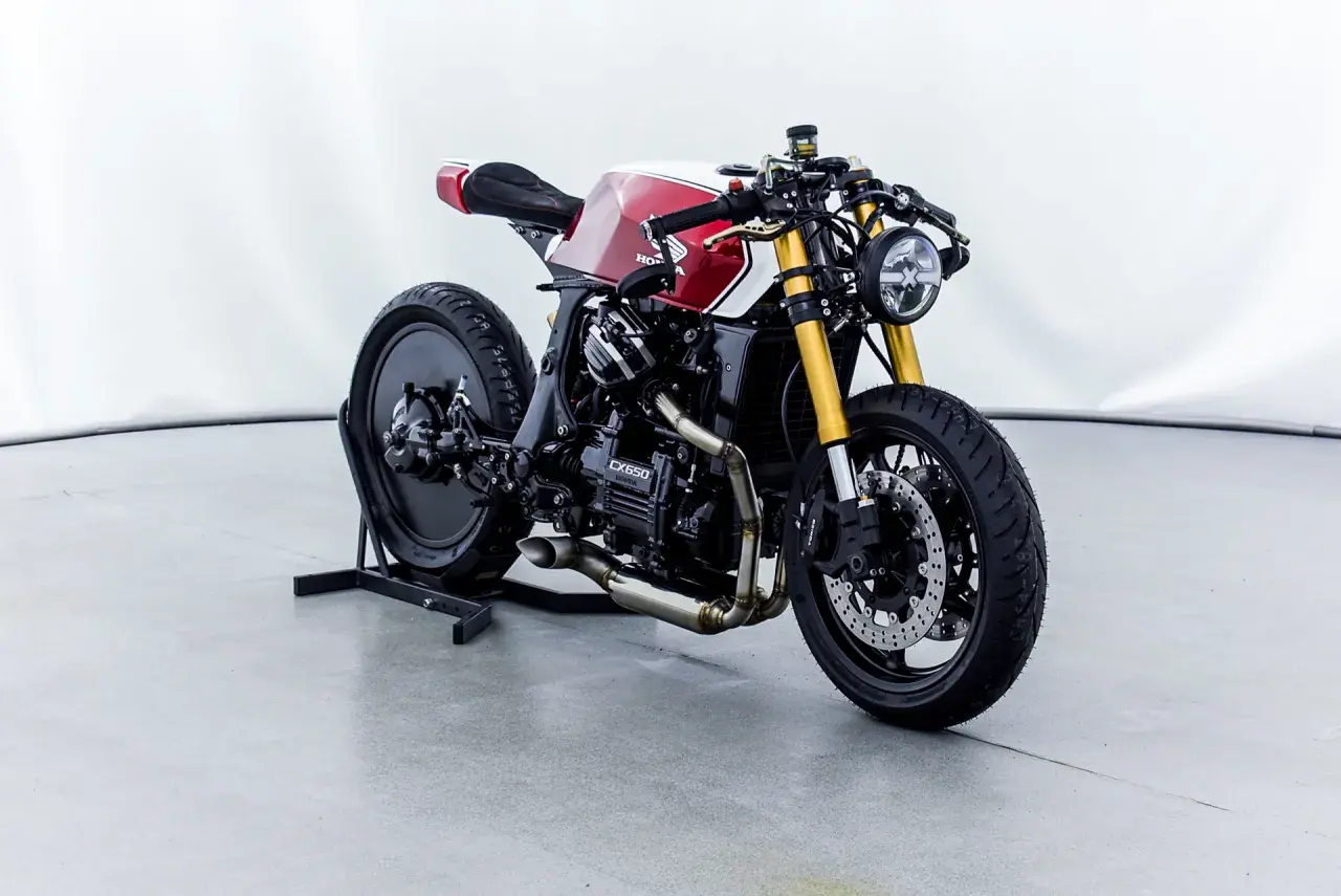 Honda CX650 custom cafe racer, rossa e bianca, con forcella dorata e scarico modificato. Un vero gioiello su due ruote.