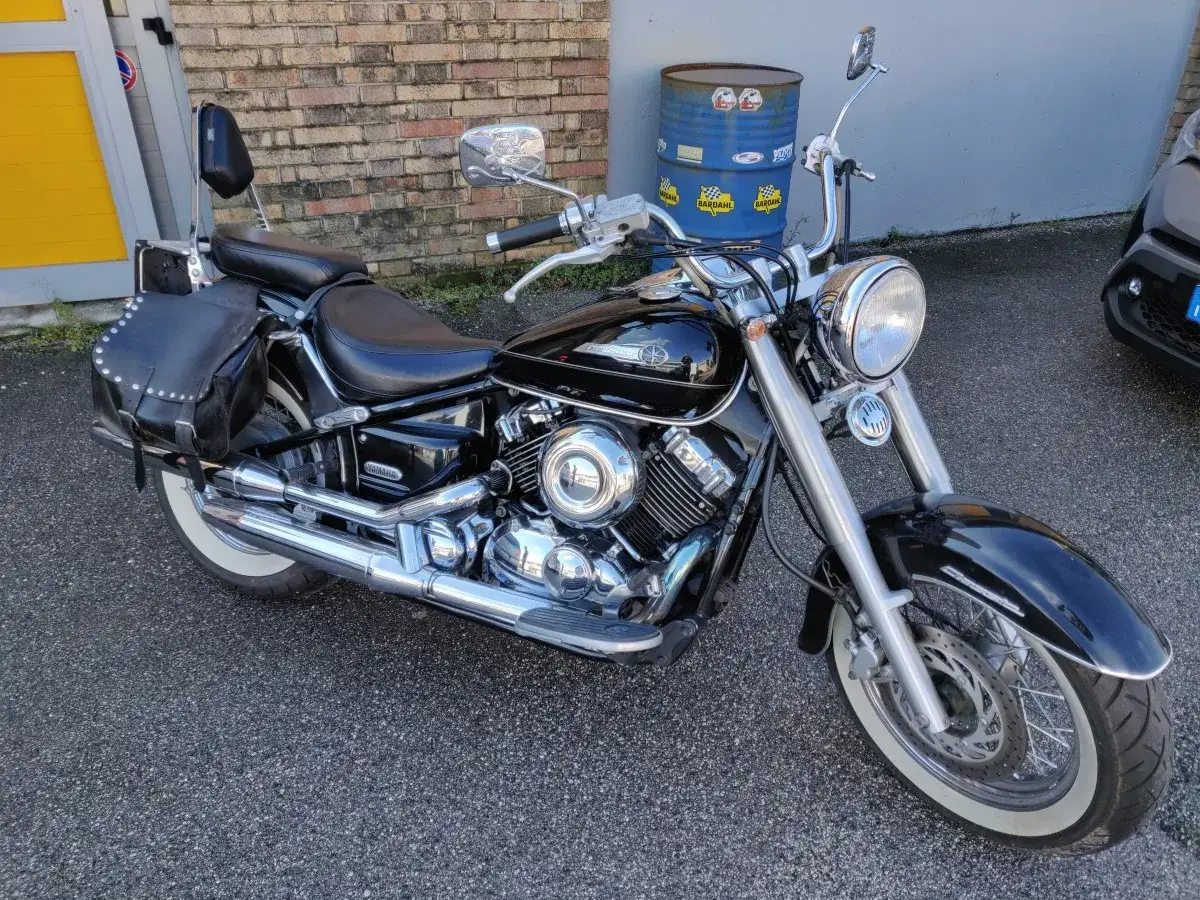 Yamaha Dragstar 650 custom nera, con borse laterali in pelle e pneumatici a fascia bianca, pronta per un viaggio.