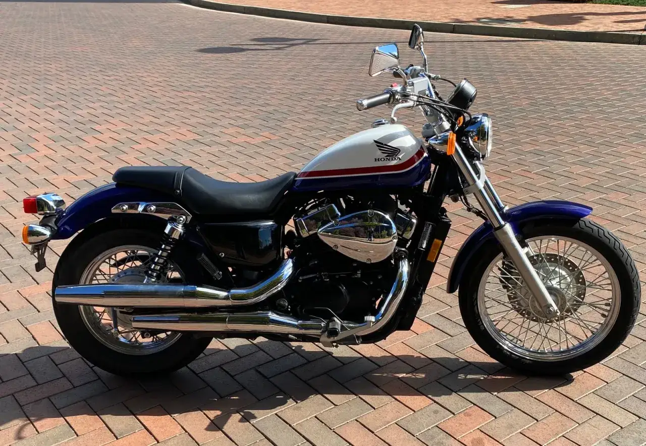 Honda VT750S blu e bianca con strisce rosse, parcheggiata su un selciato.